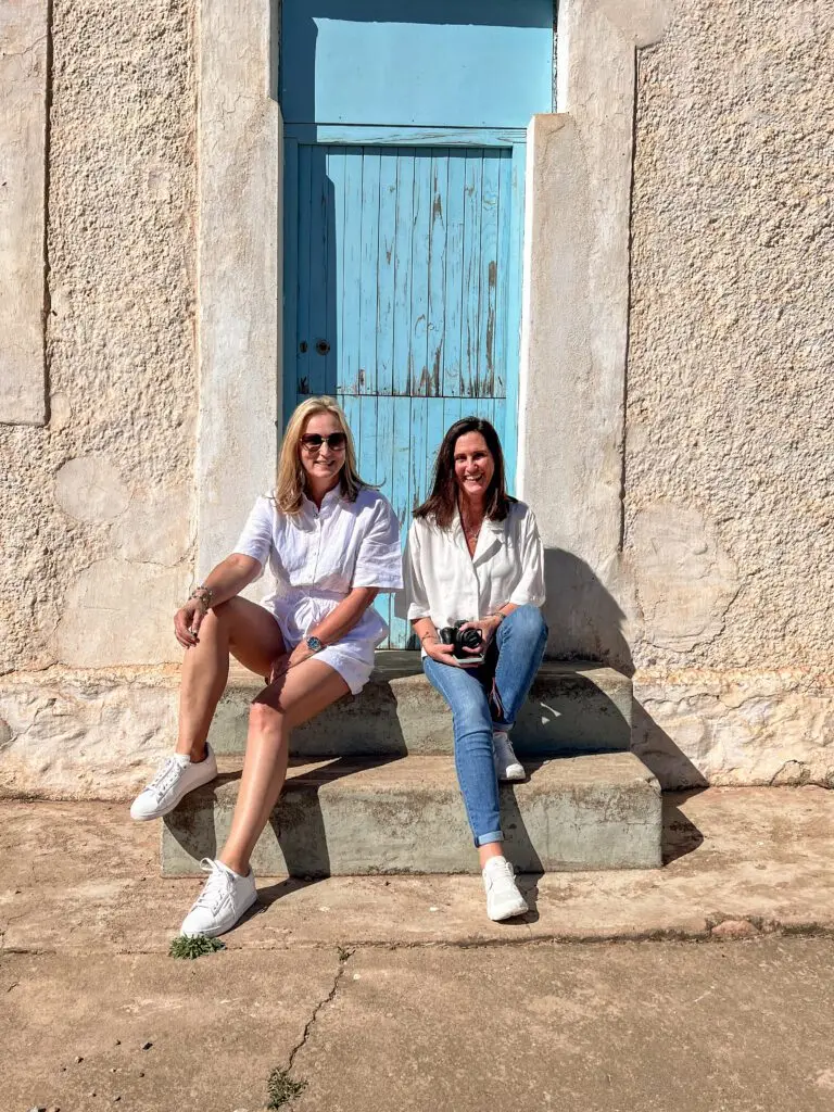 ladies sitting on the side of the road in front of an old building with turquoise door