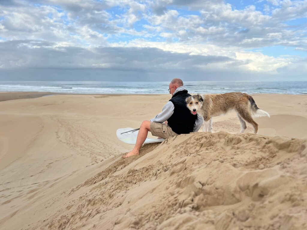 Man with dog in the sand dunes at South Africas Wild Coast.Mann mit Hund, Surfboard in den Sanddünen an der Wild Coast Südafrikas